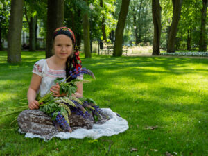 Urocza mała dziewczynka w stylizacji przedwojennej wiejskiej postaci, trzymająca kwiaty - artystyczne ujęcie przez BartiK w parku w Mławie.