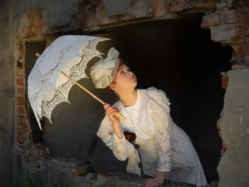 Nastoletnia Dama w przedwojennej stylizacji, ubrana w białą suknię i trzymająca parasol - wyjątkowe ujęcie przez BartiK przez wybite okno budynku.